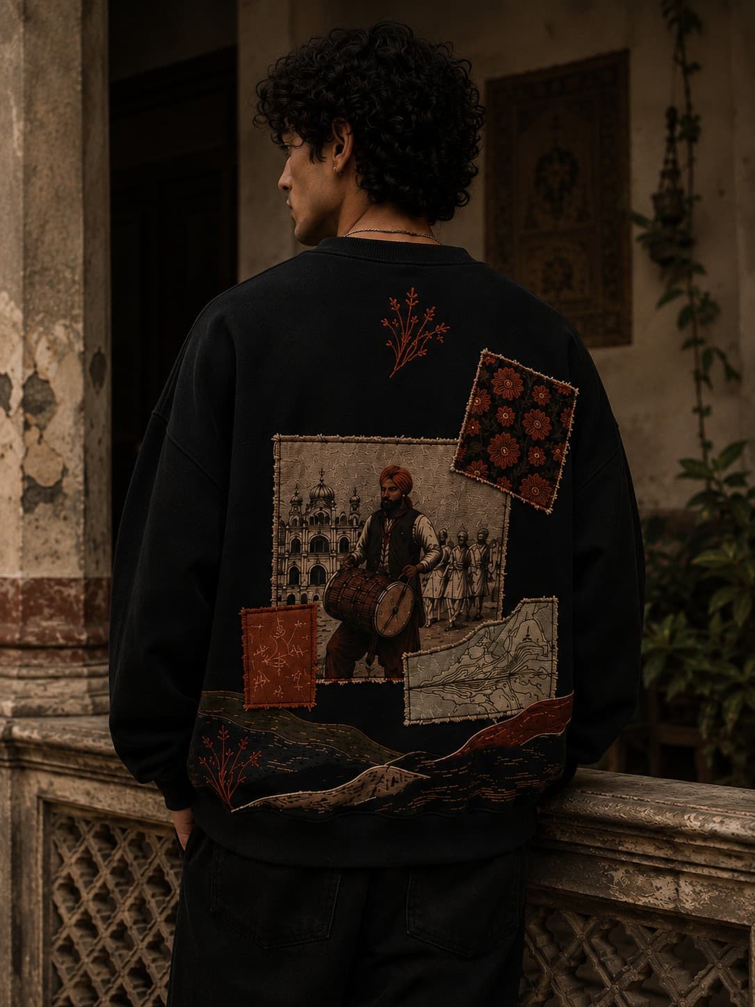 Man wearing the Sakoon black crewneck, back view, embroidered dhol drummer and shrine patchwork scene
